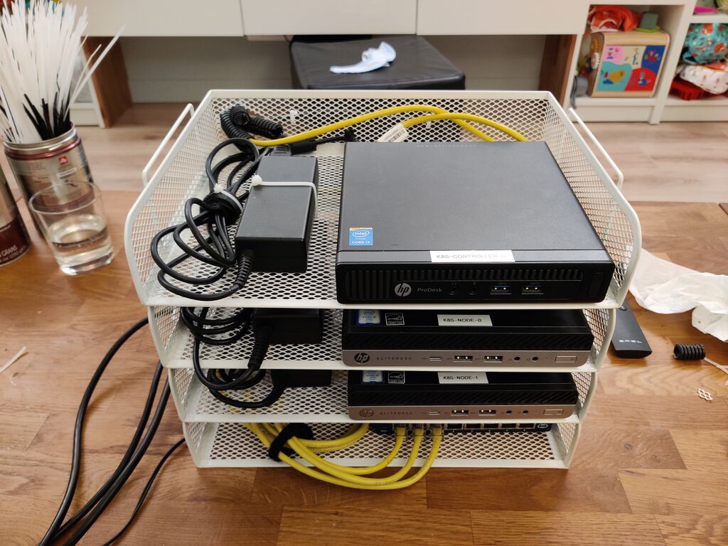 A picture of a k8s cluster built with 3 HP Minis resting on trays, cabled with a gigabit switch at the bottom tray.